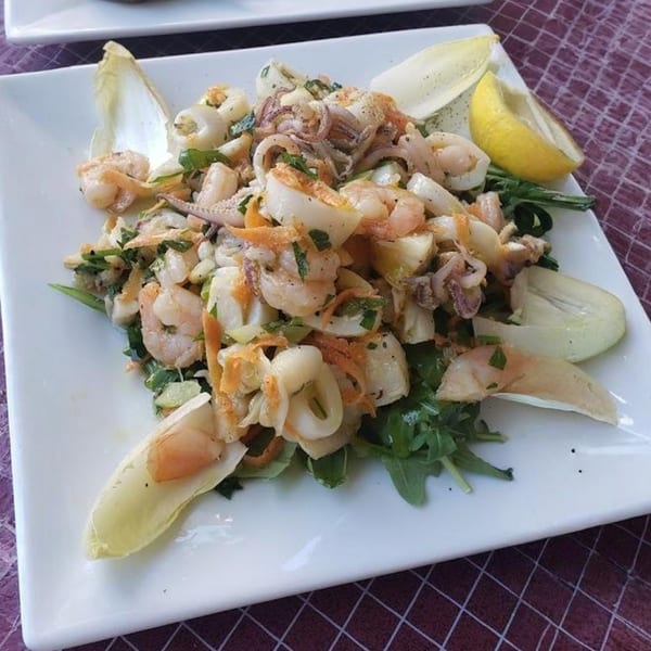 Italian seafood salad with shrimp, calamari, and greens, garnished with lemon and endive.