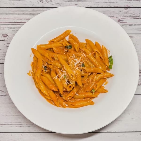 Penne pasta in a creamy orange sauce, topped with grated cheese and fresh basil, on a white plate.
