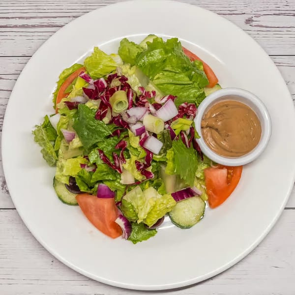 Fresh Italian salad with mixed greens, red onion, cucumber, tomato, and a side of dressing.