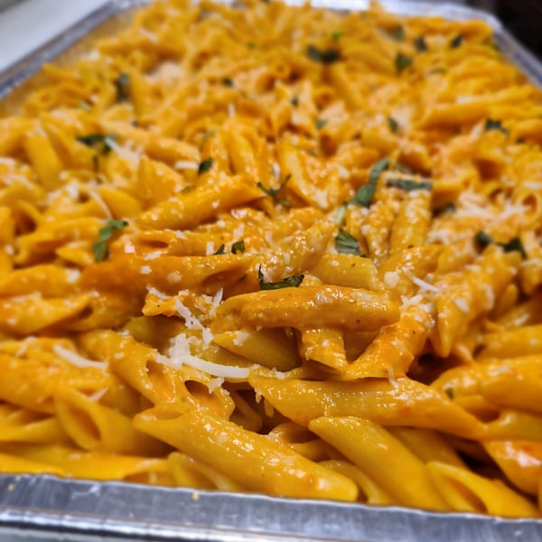 Penne pasta in a creamy orange sauce, topped with grated cheese and fresh herbs in a metal tray.