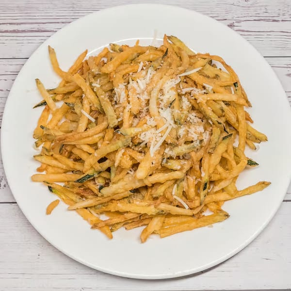 A white plate filled with golden-brown fried zucchini sticks, topped with grated Parmesan cheese.