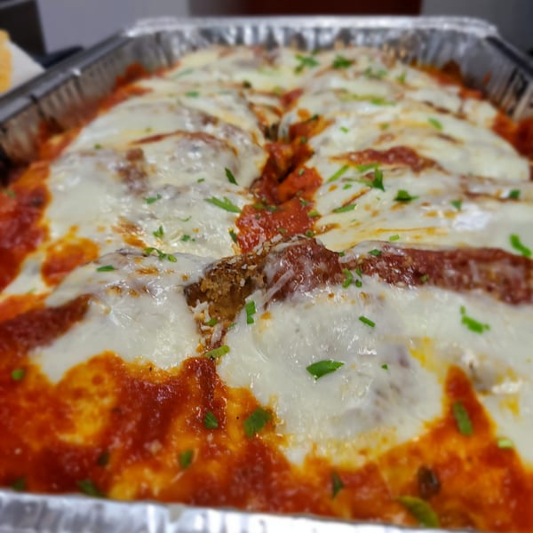 Baked Italian lasagna with melted mozzarella cheese, red sauce, and green herbs in a foil pan.
