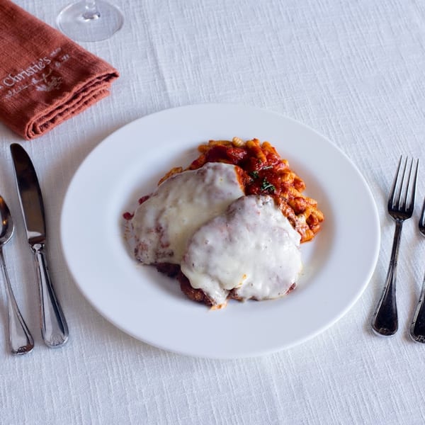 Two chicken parmesan cutlets with melted cheese and pasta in red sauce on a white plate.
