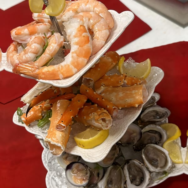 A tiered seafood tower with shrimp, crab legs, oysters, and clams on ice with lemon wedges.