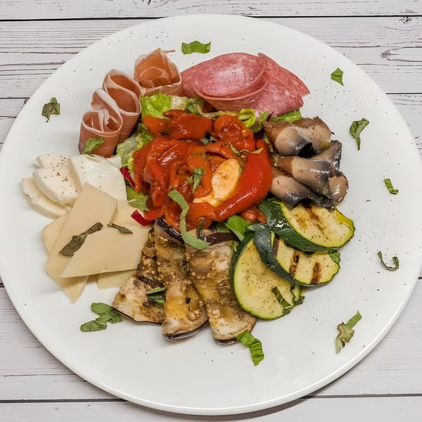 An Italian antipasto platter with prosciutto, salami, cheeses, roasted vegetables, and sardines.